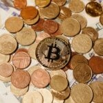 A collection of Bitcoin and various currency coins scattered on US dollar bills, symbolizing digital and traditional currency interplay.